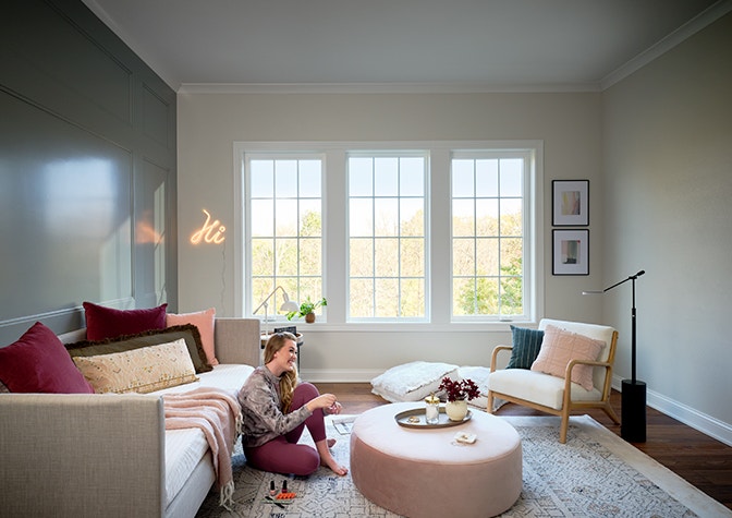 three white casement windows on the far side of a soft pink- and teal-colored living room.