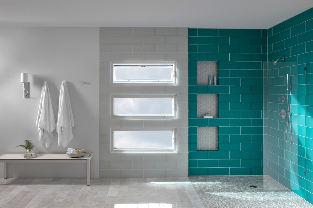 Teal tile shower next to a stack of three awning windows with the top window vented