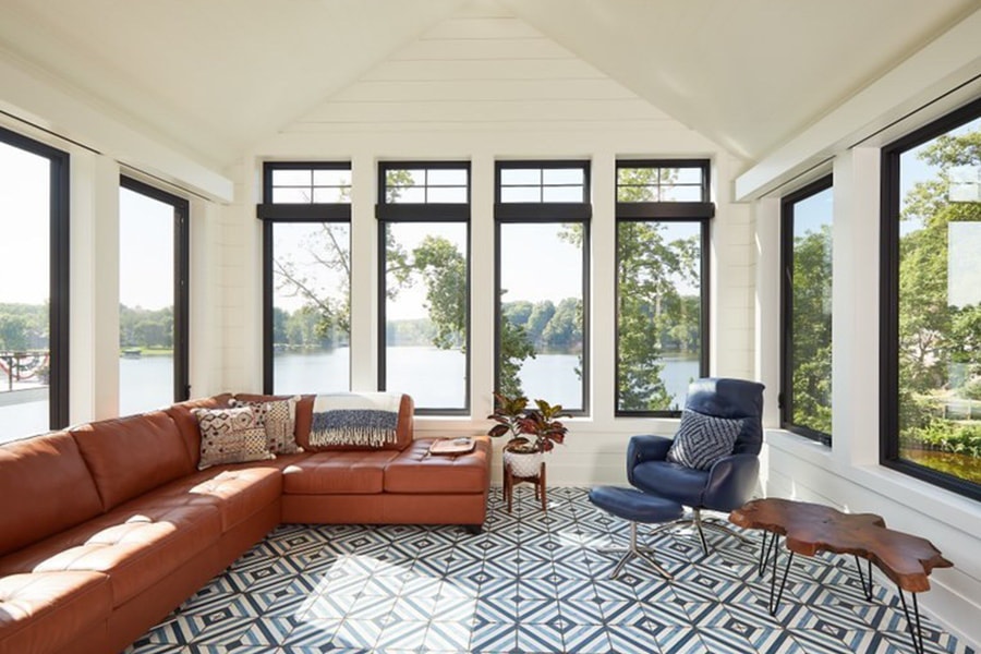 A sunroom that looks out onto a lake, featuring black-trimmed windows surrounding a burnt orange corner section.