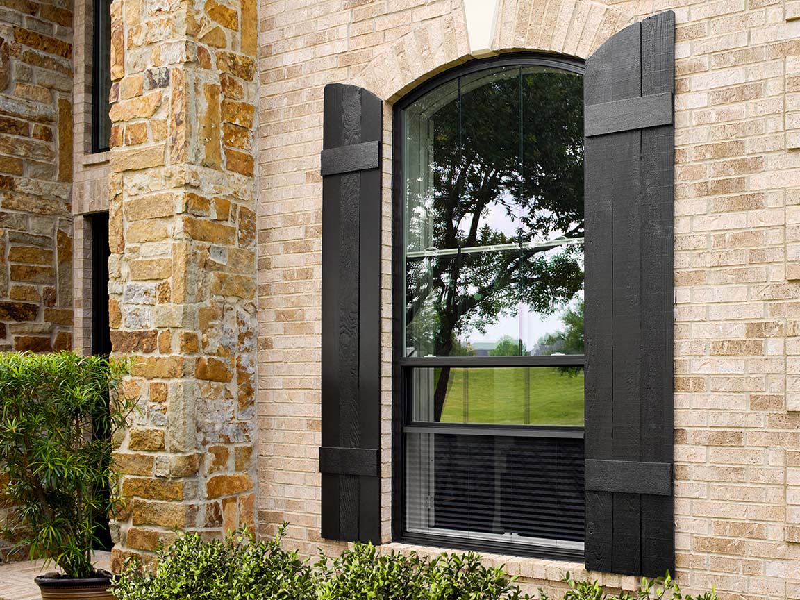 Arched window with black shutters on stone and brick home exterior.