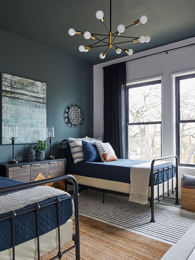 Modern bedroom with black-framed windows, twin metal beds, and navy and neutral decor.