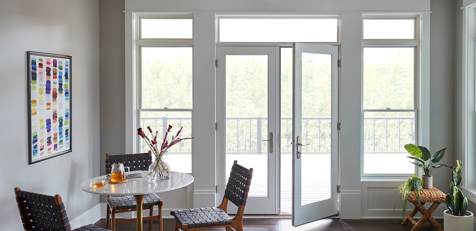 A white french door with silver hardware opens to a deck and is flanked by white double-hung windows.