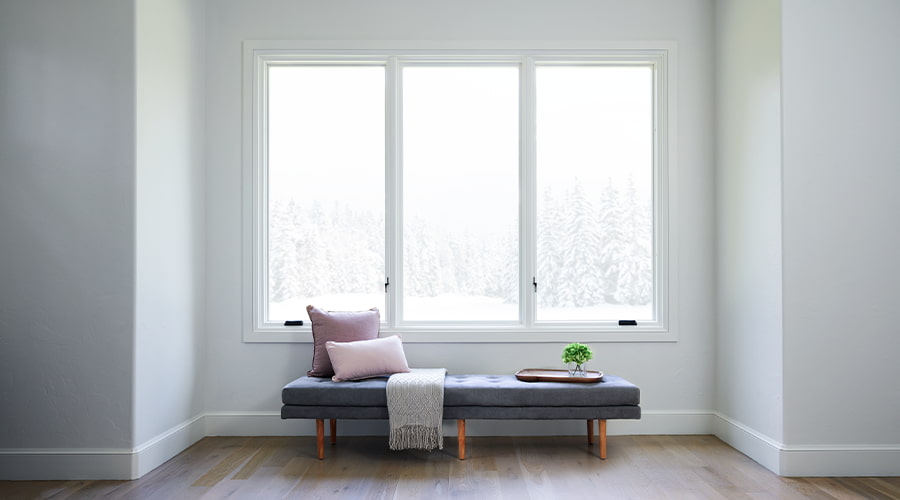 three white casement windows over a blue window bench looking out into a winter snowscape