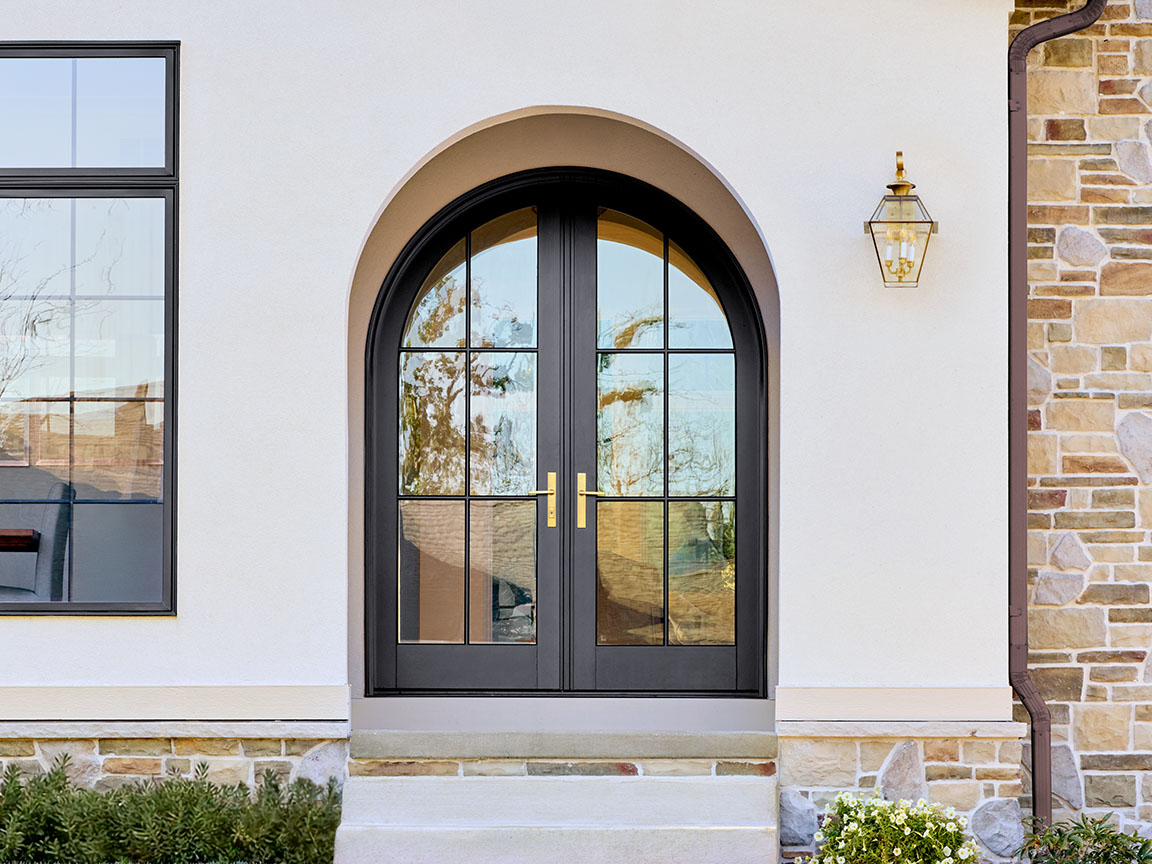 Arched black French entry door with glass panels on a stone-accented exterior.