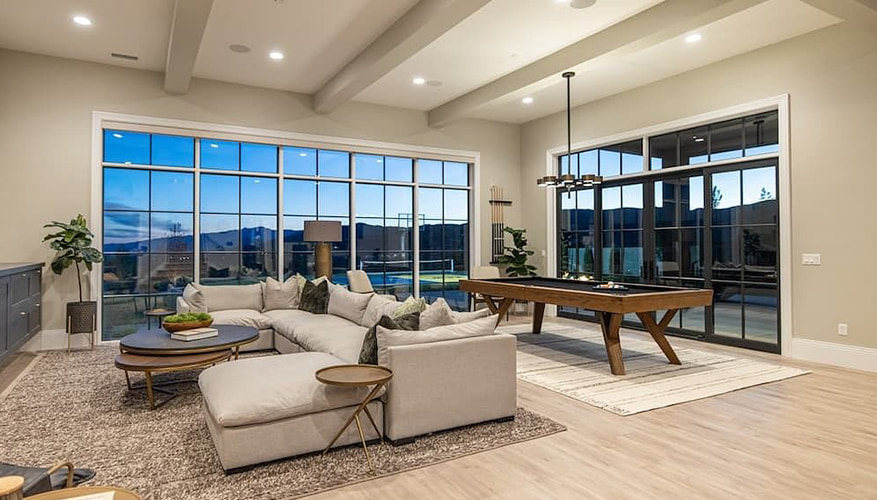 A family and game room at dusk view through the floor-to-ceiling and french doors on the far walls