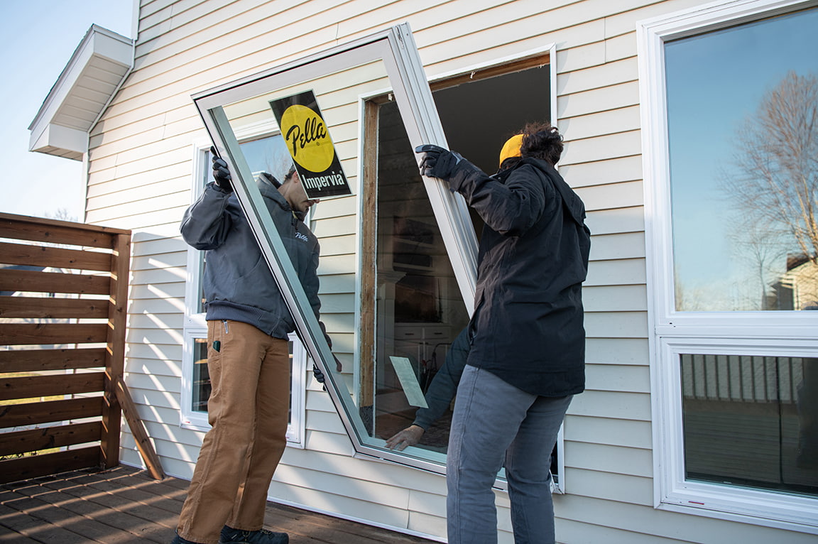Two workers installing a Pella Impervia replacement window in a house, demonstrating replacing a replacement window.
