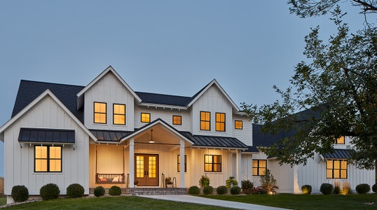 Large White Home with Lit Windows and Wood Entry Door