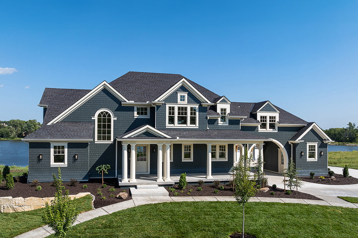 A modern home exterior with a lake view, featuring hidden screen windows and landscaped yard.