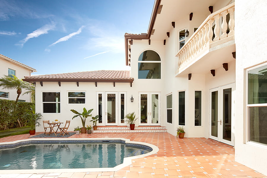 Exterior white home with white Hurricane Shield patio doors, red tiled outdoor space and pool