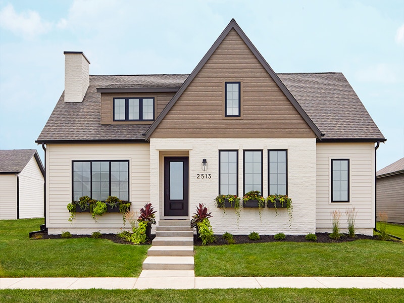 window boxes with a wide variety of flowers and green plants sit below several front windows on a white brick home