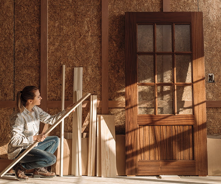 a female contractor assesses wood pieces next to a new wood entry door