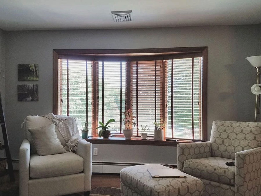 A living room featuring a before bow window with white chairs and plants, showcasing natural light.