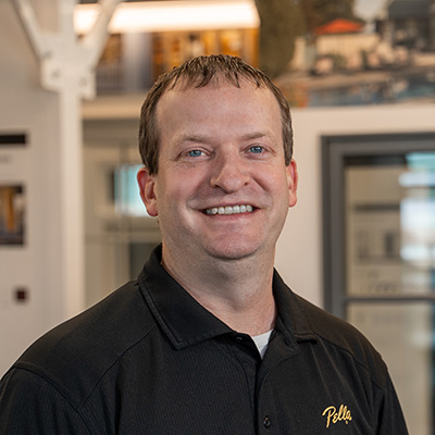 A Pella team member is wearing a black shirt and standing in front of floor displays of Pella products.