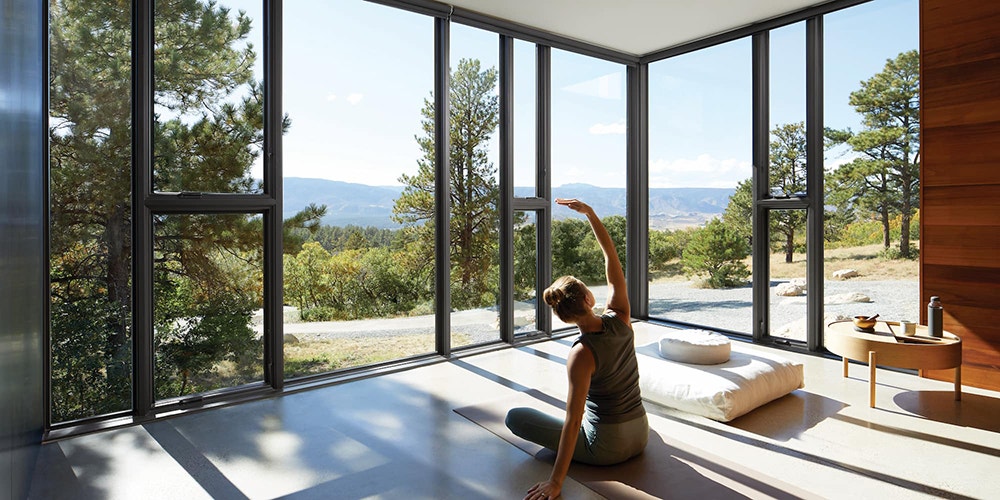 black floor-to-ceiling windows and sliding doors open to a lush green mountain view