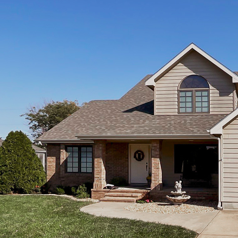 A before view of a home exterior featuring a sloped roof and casement windows, surrounded by greenery.