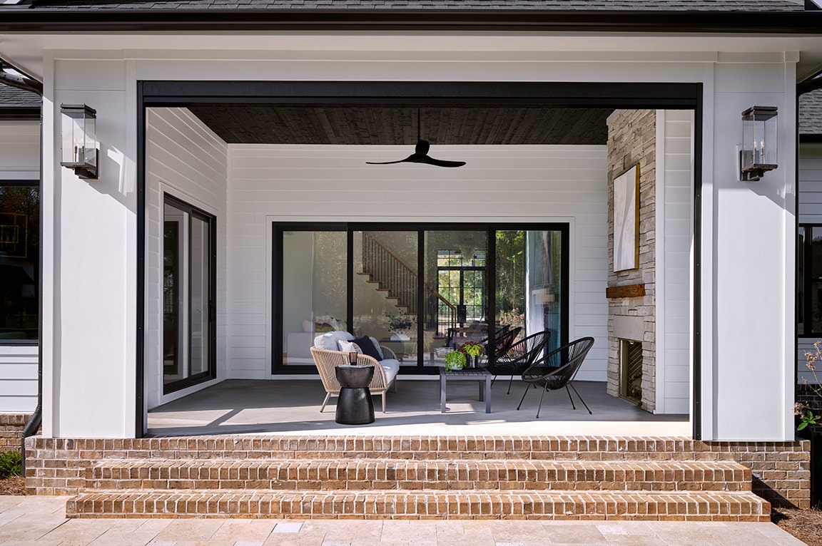 Black frame patio doors open to a covered patio with brick steps and modern outdoor seating.