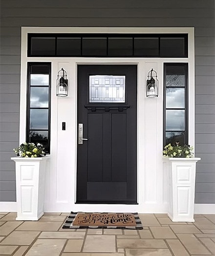 A front entrance features a black front door with decorative glass on the top portion along with sidelights and planters on both sides.