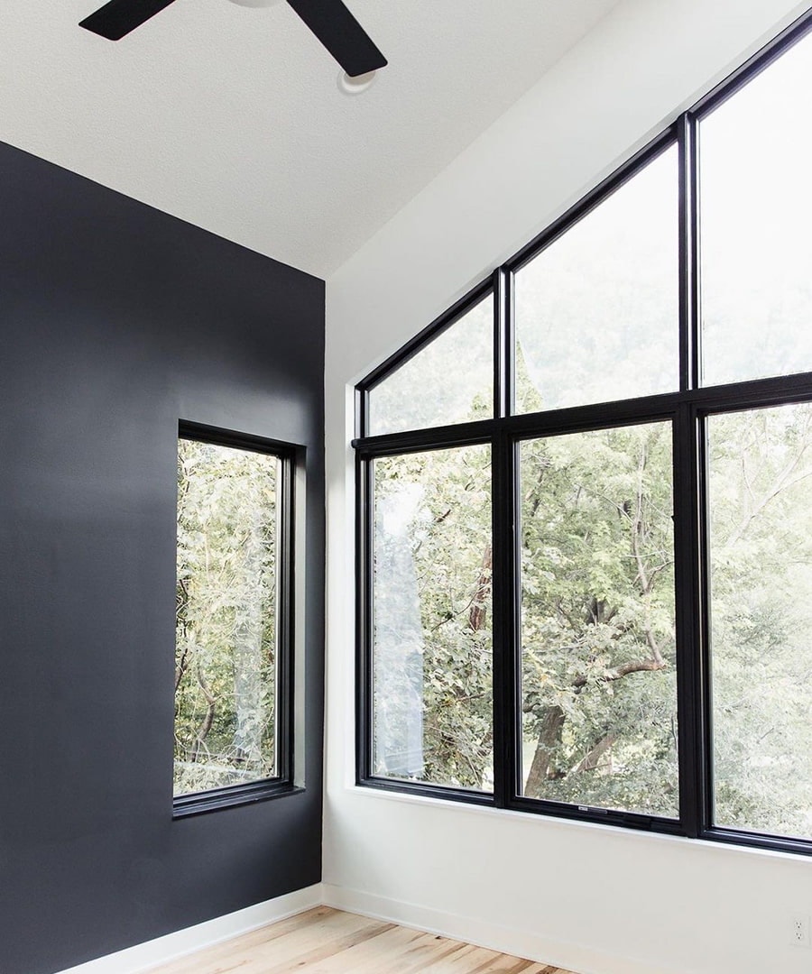 A white wall features a custom shape black window that aligns with the shape of the roofline.