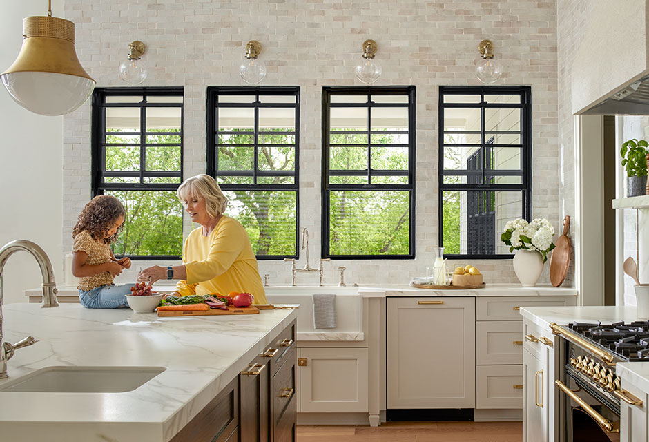 Two people are cooking food at a large island in front of four black double-hung windows with hidden screens that let in the fresh air.