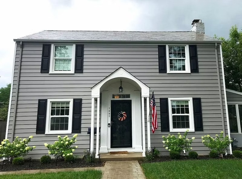 A gray colonial home exterior that includes white single-hung windows with black shutters