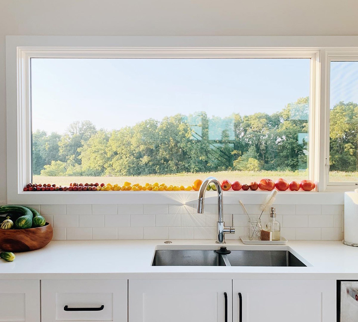 A white rectangular window over the kitchen sink acts as a shelf for resting an array of colorful produce.