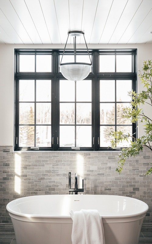 White bathtub with black bathroom window and a plant beside it