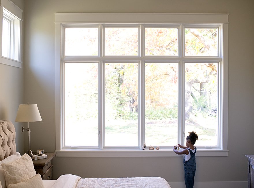 Girl playing with toys by painted white windows with white trim in bedroom