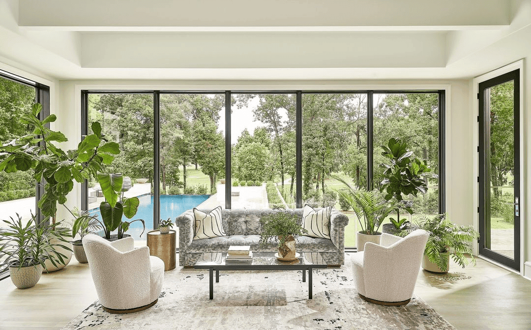 A room with plants and chairs features sunroom windows and a patio door from floor to ceiling.