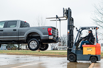 a gray pickup truck is being suspended in air from a fiberglass window frame that is on forklift forks.