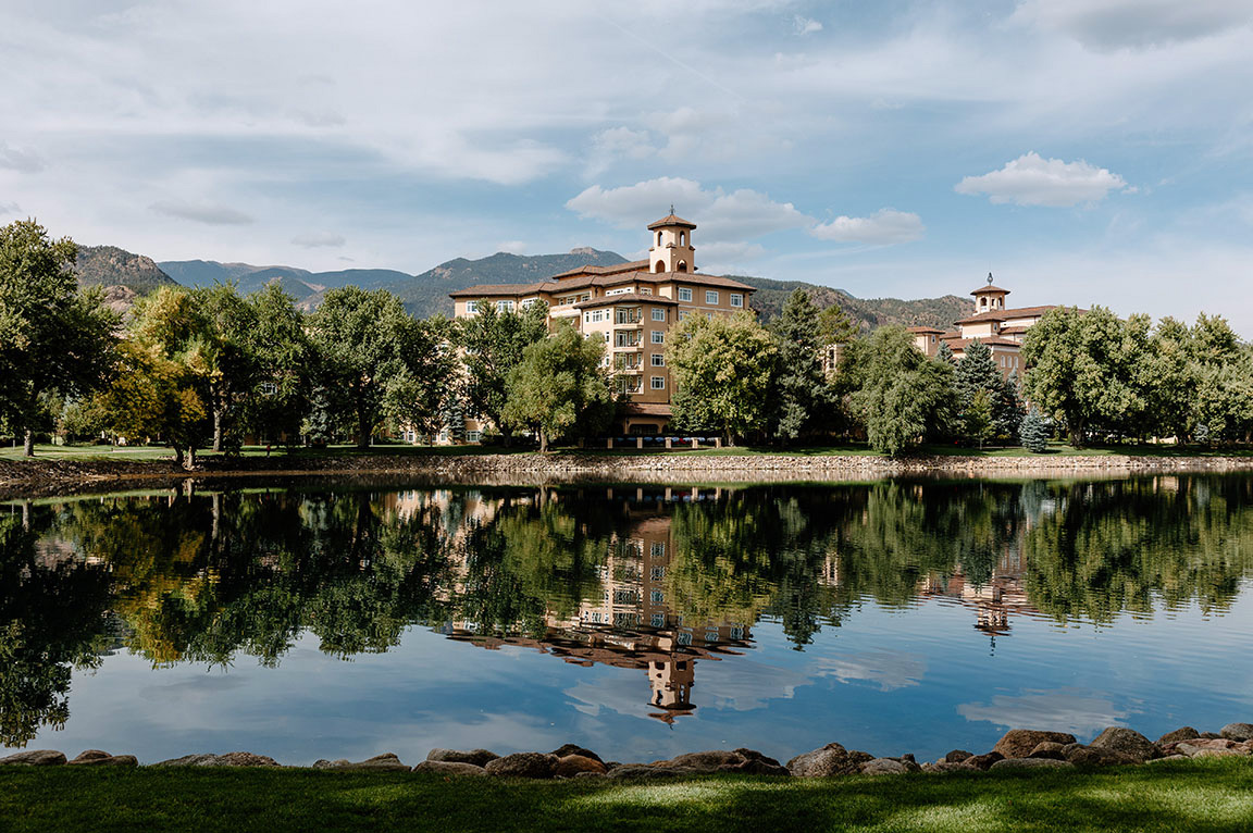 A scenic view of a lake reflecting a building surrounded by trees, featuring casement windows.