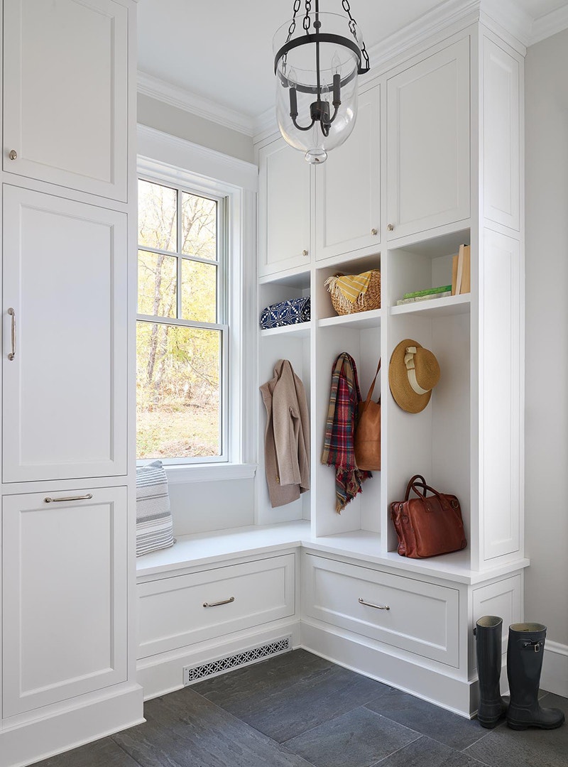 A white mudroom is brightened by a white double-hung window between the storage cabinets.