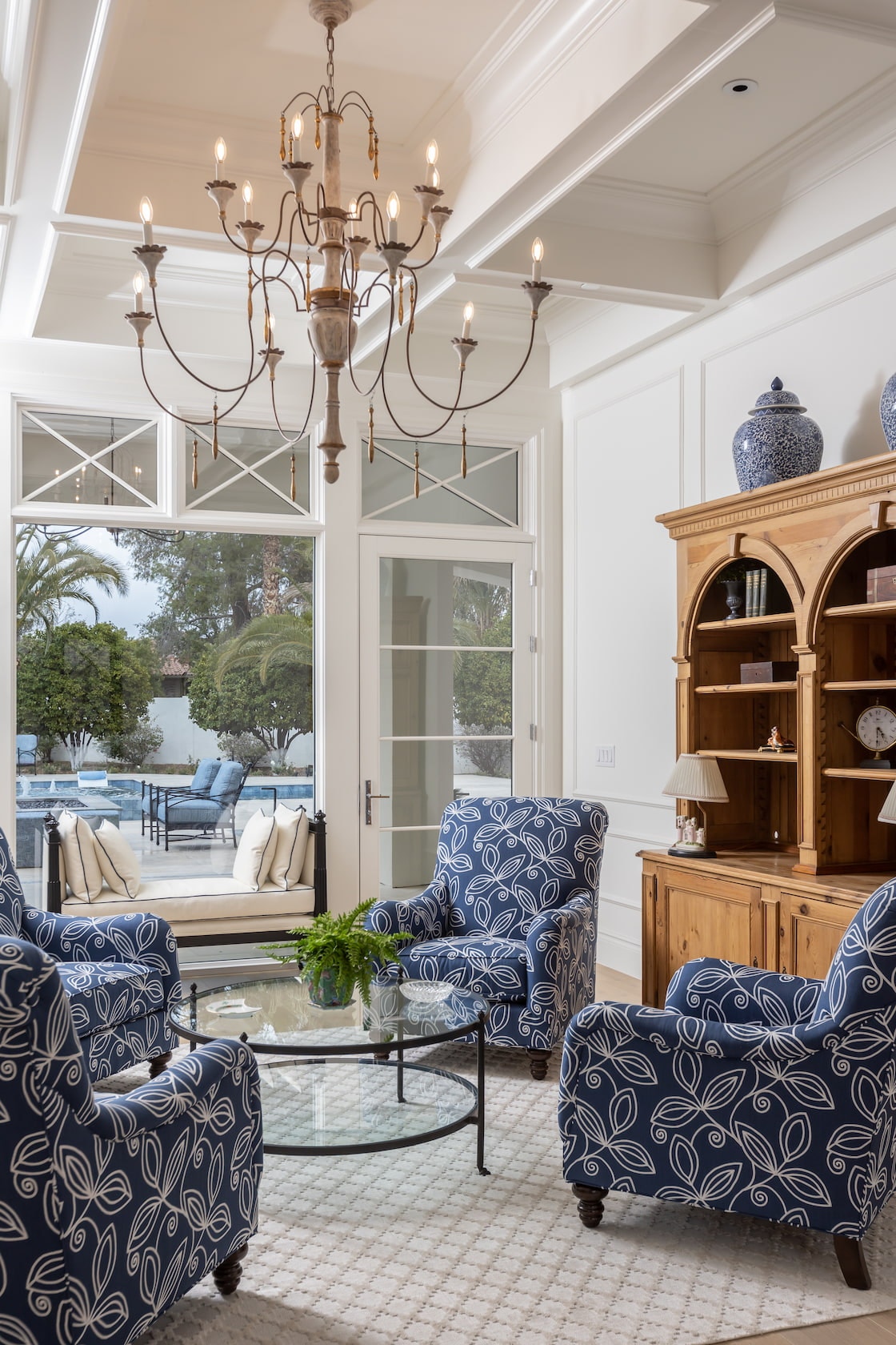 An Arizona living room with blue chairs and a chandelier features a custom hinged door and white windows.