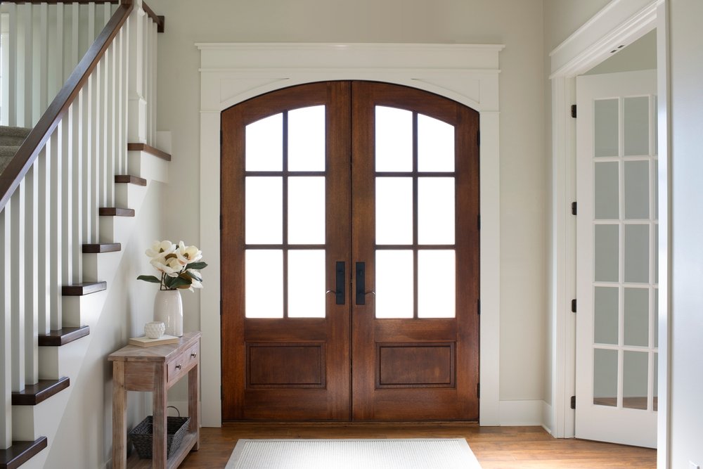 White interior entryway with a wood double door with an arched top and traditional grilles on the 3/4 glass