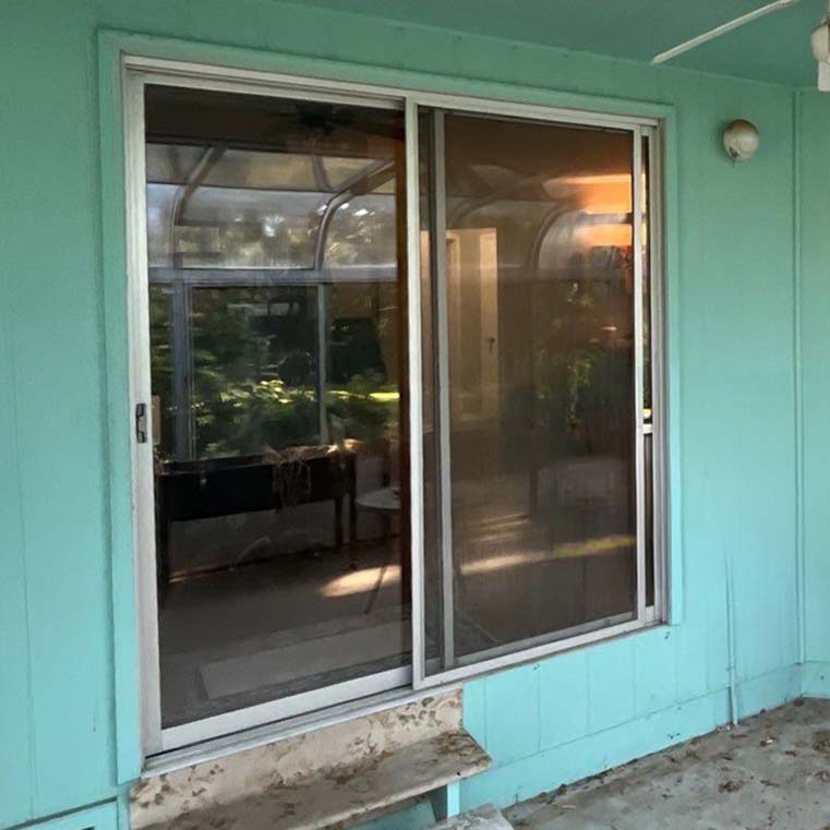 Turquoise patio wall with sliding glass door and screen reflecting sunroom and backyard foliage, chipped concrete step below