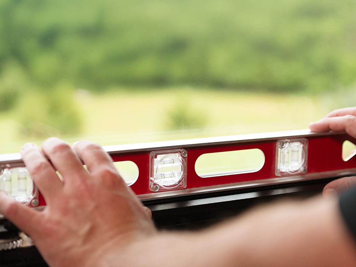 Someone is using a large level to test a newly installed window and making sure it is not slanted.