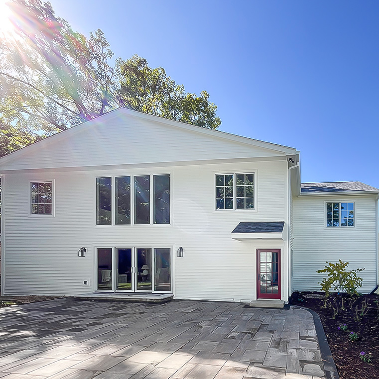 Modern two-story home with white siding, large windows, and stone patio under clear blue sky.