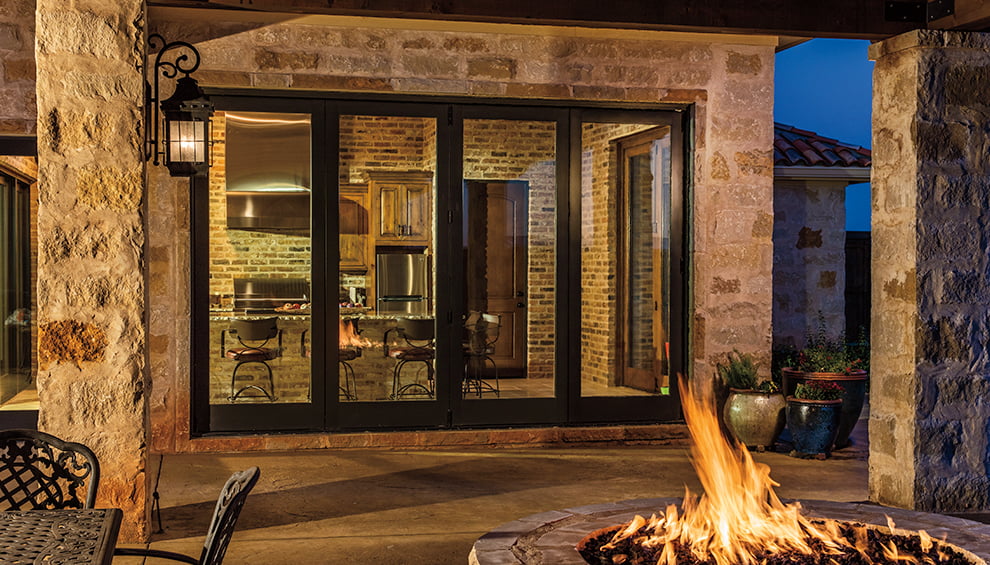 four-panel multi-slide patio door on a brick home opening to an outdoor deck with a firepit.