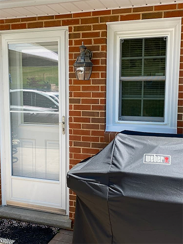 covered grill under a white window and next to a white front entry door with a white storm door
