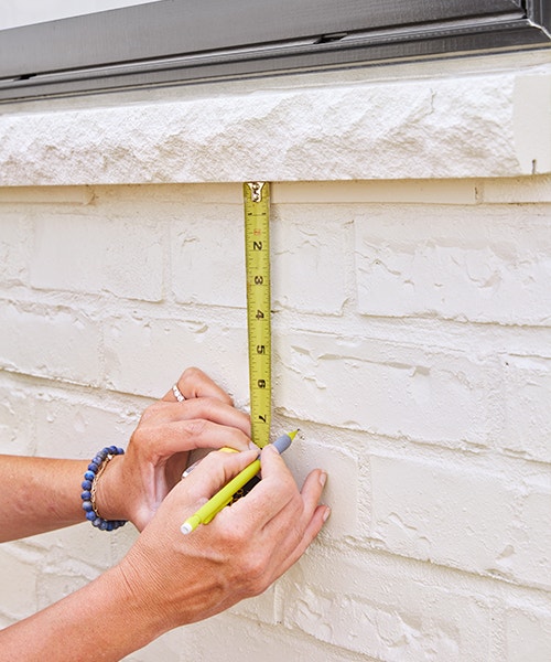 Using a tape measure to find the correct spot on an exterior wall and marking the spot with a pencil.