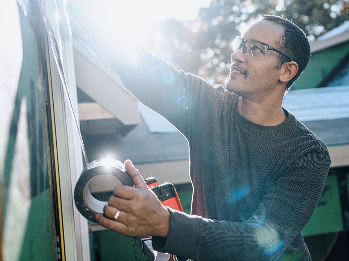 A Pella installer is adding installation tape around a newly installed window.