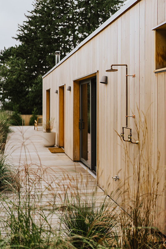 A modern home with wood siding and large energy efficient windows overlooking a landscaped garden.