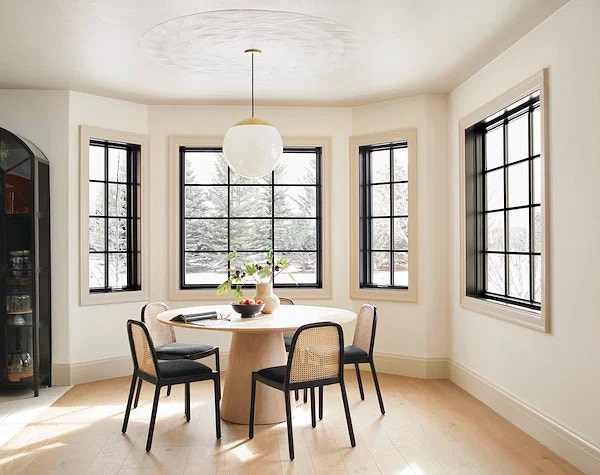 four black windows with traditional grilles surround a retro dining room table