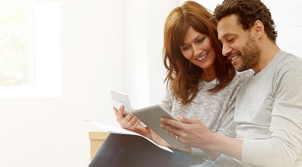 man and woman smiling while looking at a computer tablet