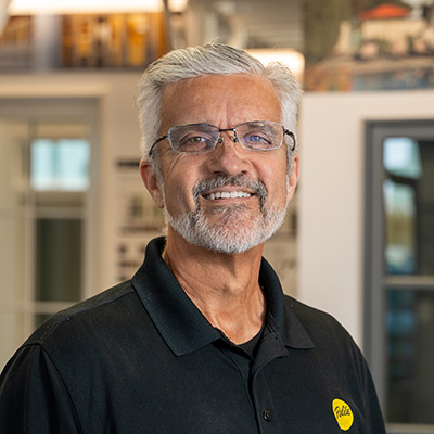 A man with glasses and gray hair and beard is wearing a Pella shirt and smiling at the camera lens.