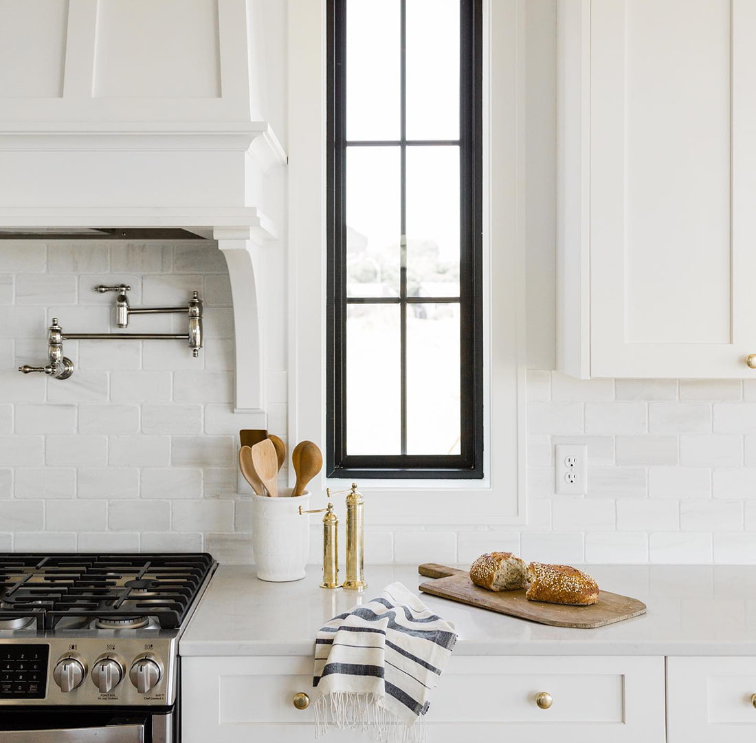A rectangle picture window sits between the hood of the stove and kitchen cabinets.