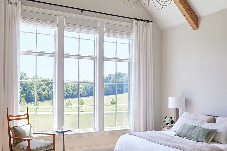 three white casement windows with white drapes in a rustic bedroom