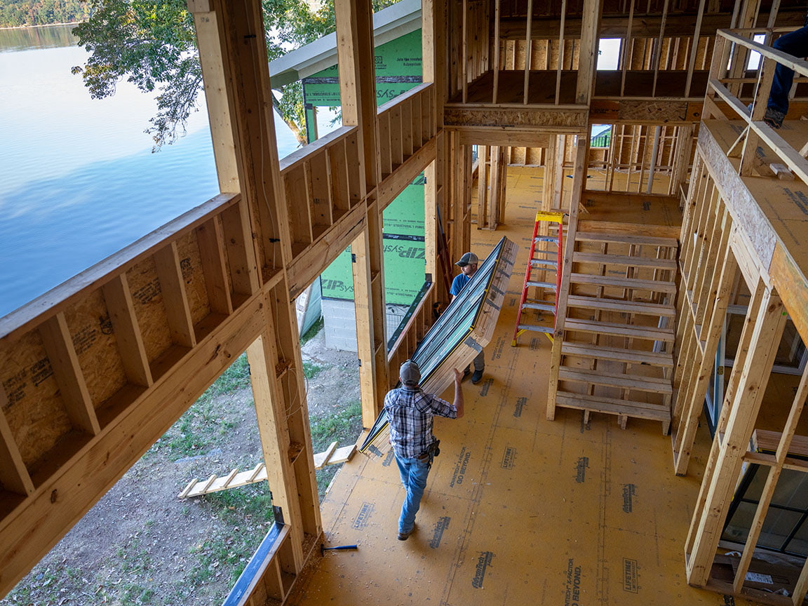 Two contractors on a jobsite are carrying a new window to the place it will be installed.