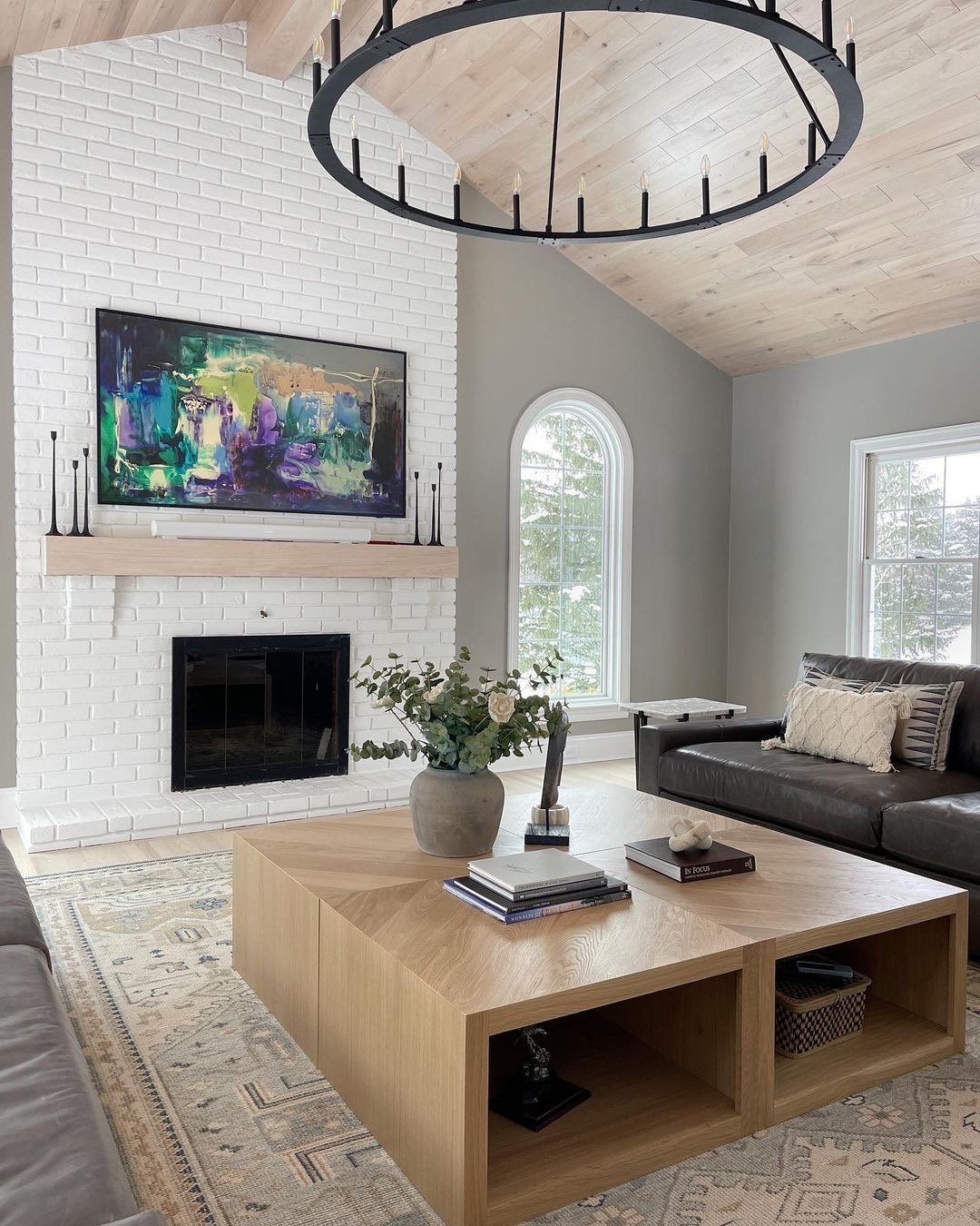 A living room has a white arch window to the right of the white fireplace.