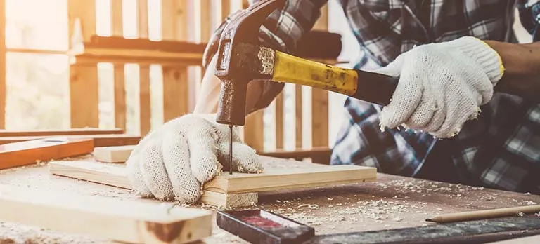 Hands hammering a nail into wood.