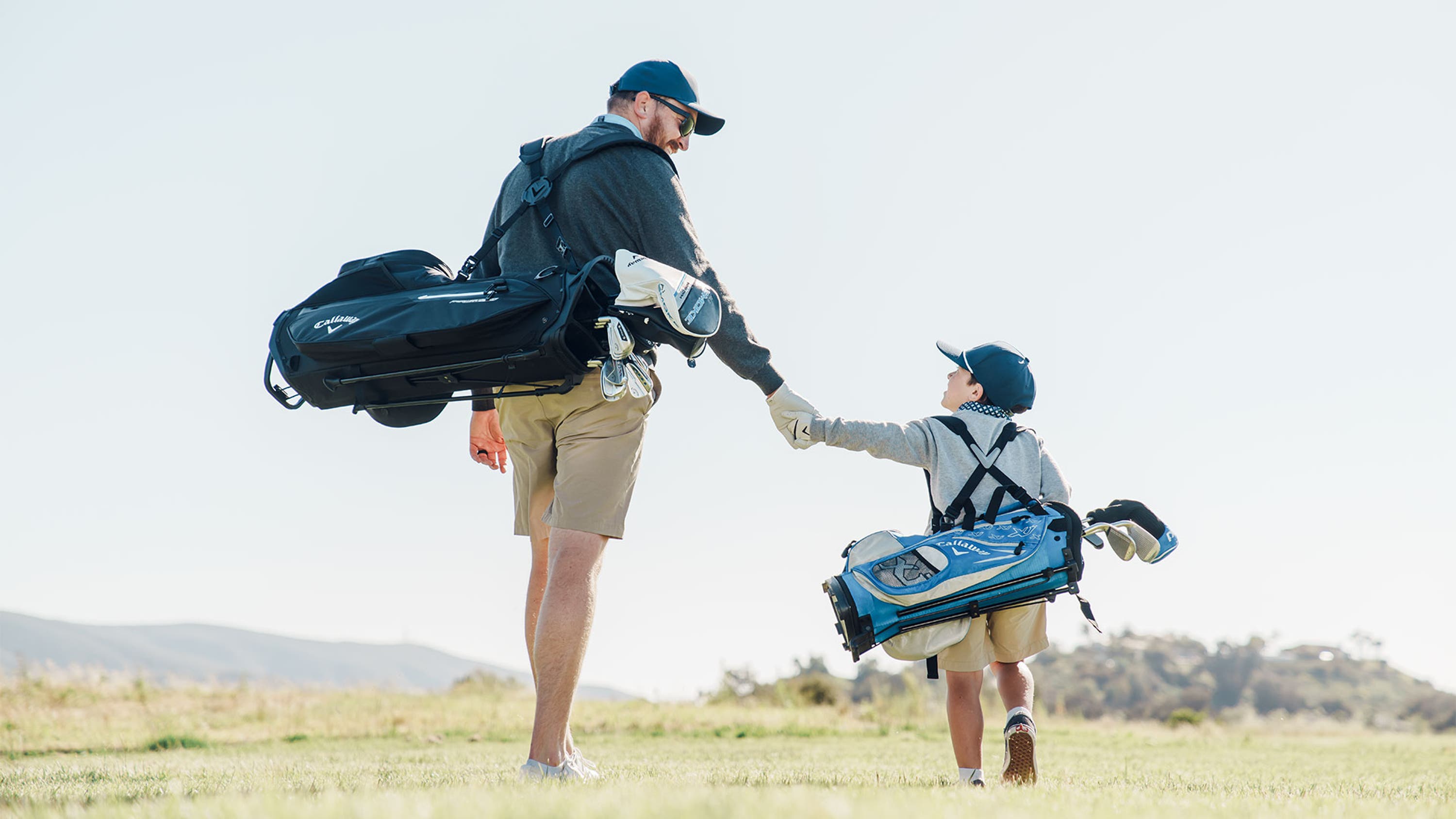 Father and son duo walking hand in hand each carrying their bag full of golf clubs